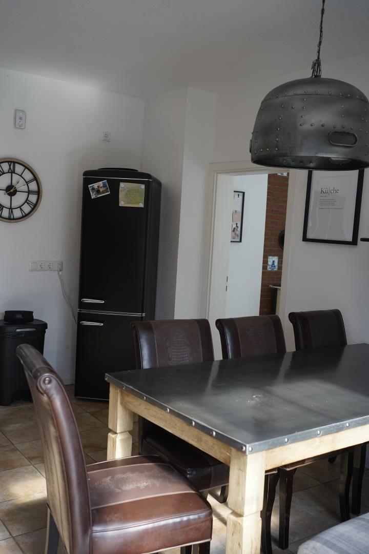 Dining area with table, chairs, and refrigerator. Hanging lamp and wall clock visible.