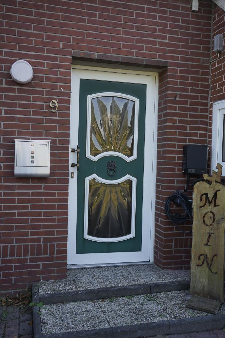 Entrance door with green frame and glass panels. Wooden sign with lettering stands beside it.