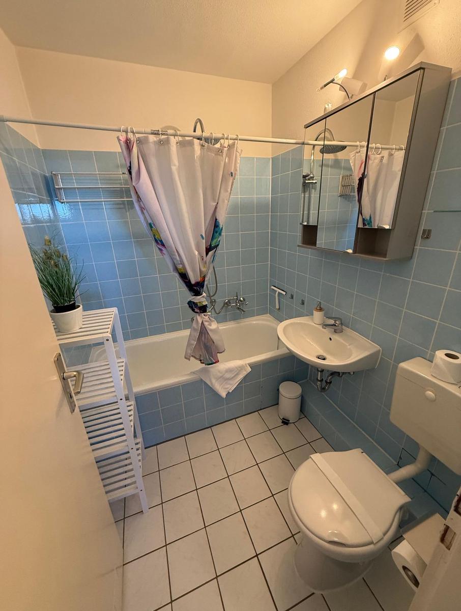 Badezimmer mit Badewanne, Waschbecken und Toilette. Blaue Fliesen und weißer Boden.