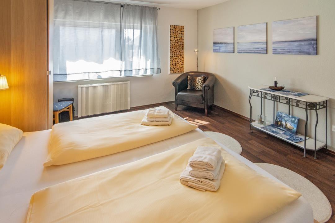 Zimmer mit zwei Betten, Sessel und Wandbildern.