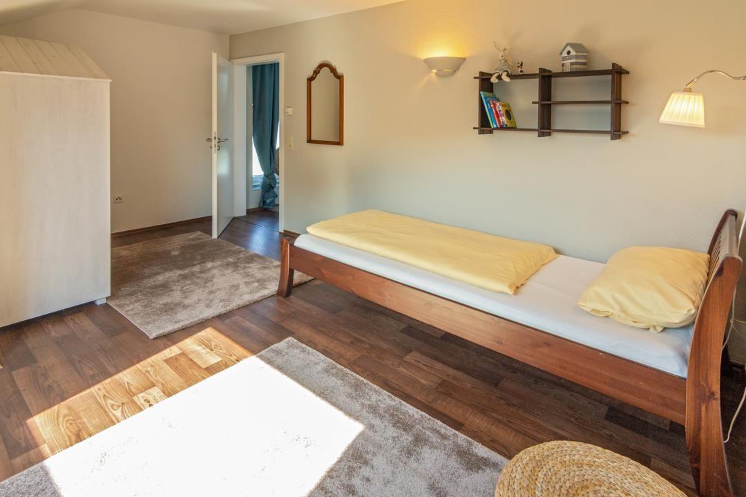 Ein Schlafzimmer mit Holzboden, Bett und Regal an der Wand.