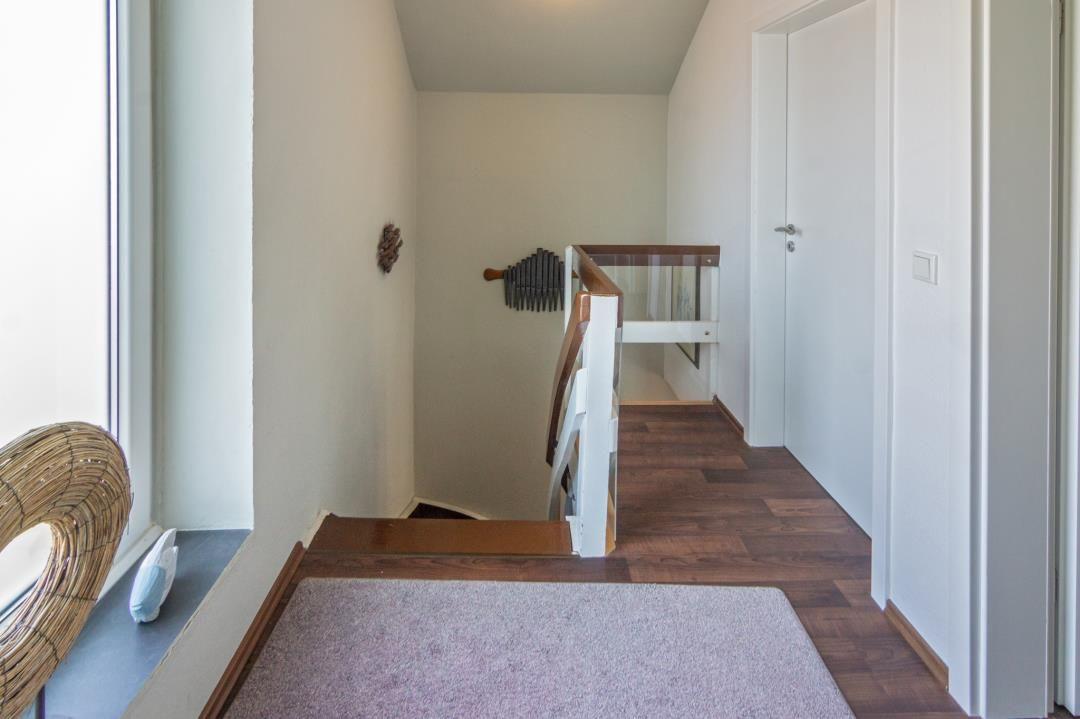 Hausflur mit Holzfußboden, Treppe und Fenster. Wanddekoration und Tür sichtbar.