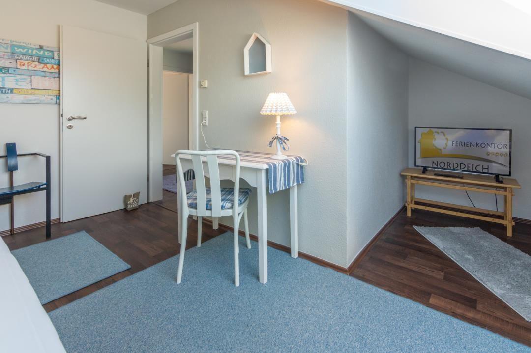 Zimmer mit Schreibtisch, Stuhl, Fernseher und Holzboden.