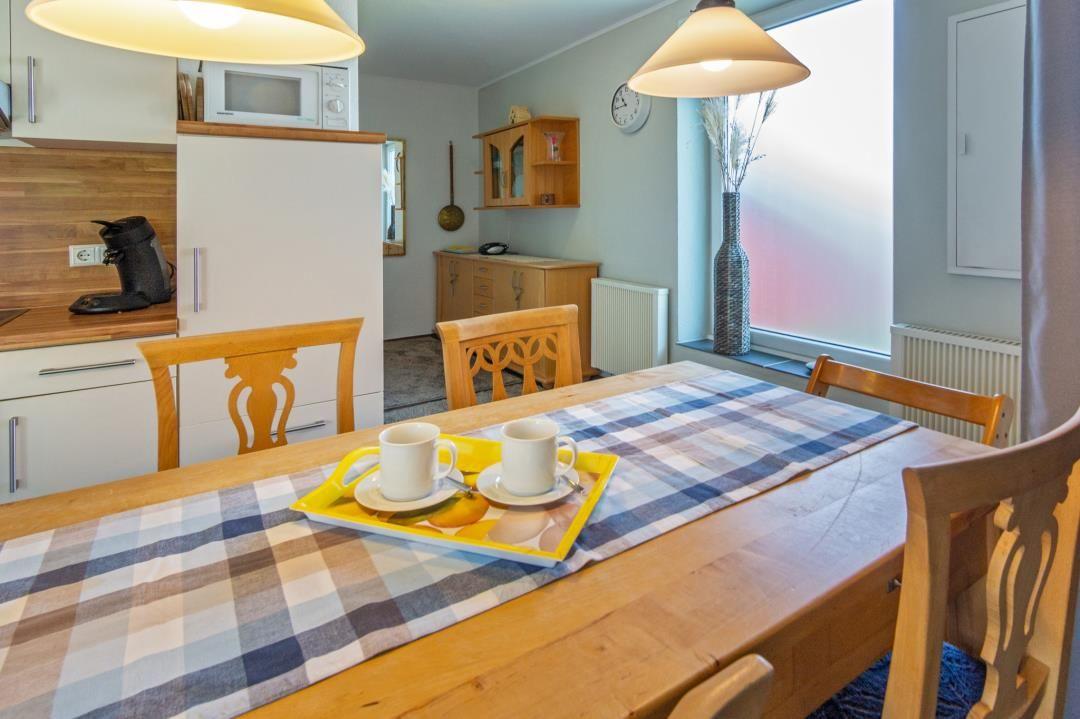 Esszimmer mit Holztisch, Stühlen und Küchenbereich im Hintergrund.