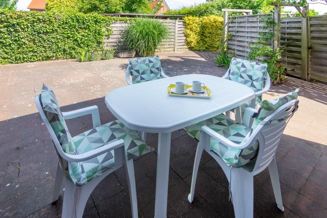 Terrasse mit weißem Tisch und vier Stühlen mit Kissen.