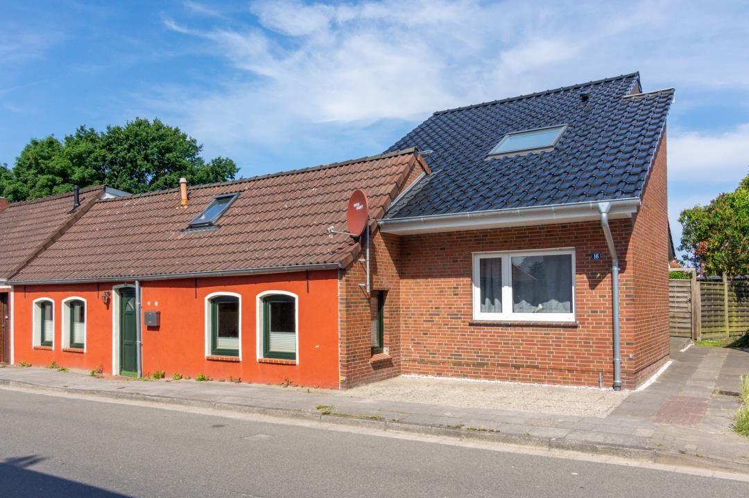 Ein zweistöckiges Haus mit rotem und braunem Dach, Fenstern und einer Terrasse.