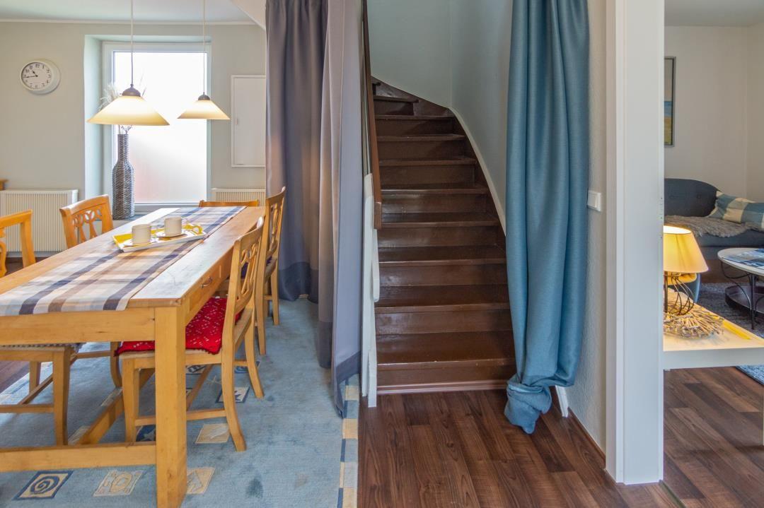 Essbereich mit Tisch, Stühlen und Tischdecke. Treppenhaus mit Holztreppe und Vorhängen.