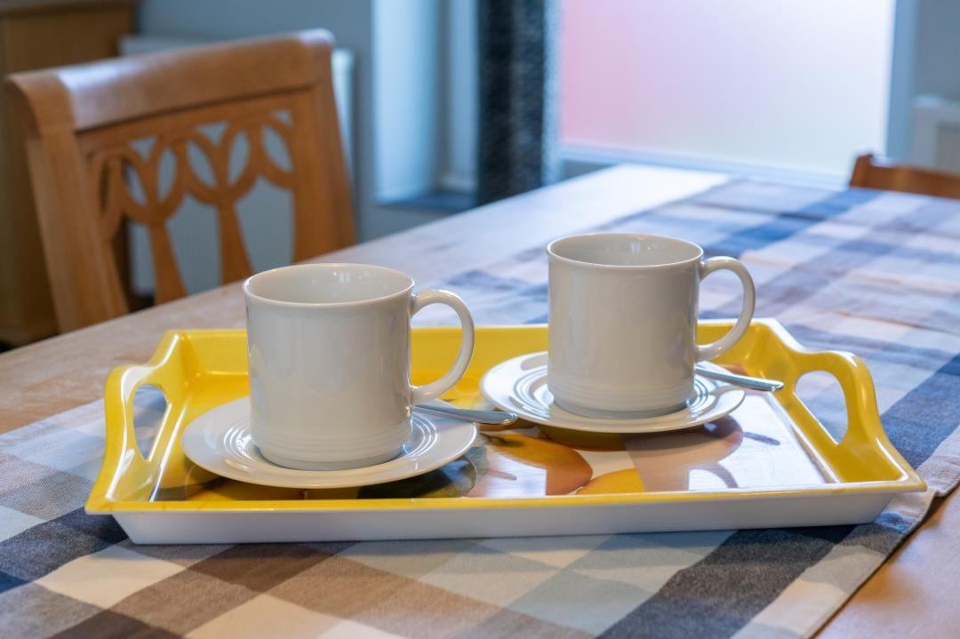 Gelber Tablett mit zwei weißen Tassen auf gemustertem Tisch