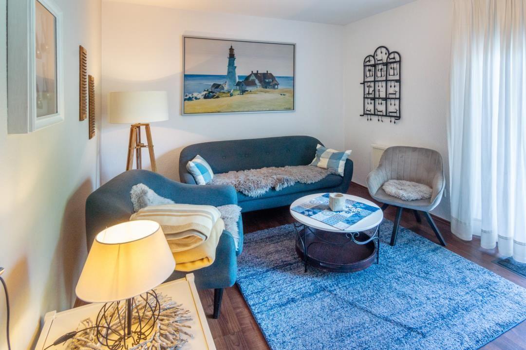 Wohnzimmer mit Sofa, Sessel und Tisch auf blauem Teppich