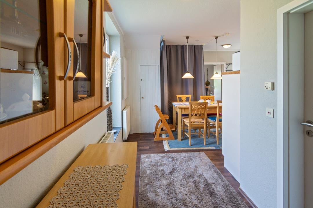 Küche mit Holzschränken, Essbereich mit Tisch und Stühlen, Teppich und Vorhänge.