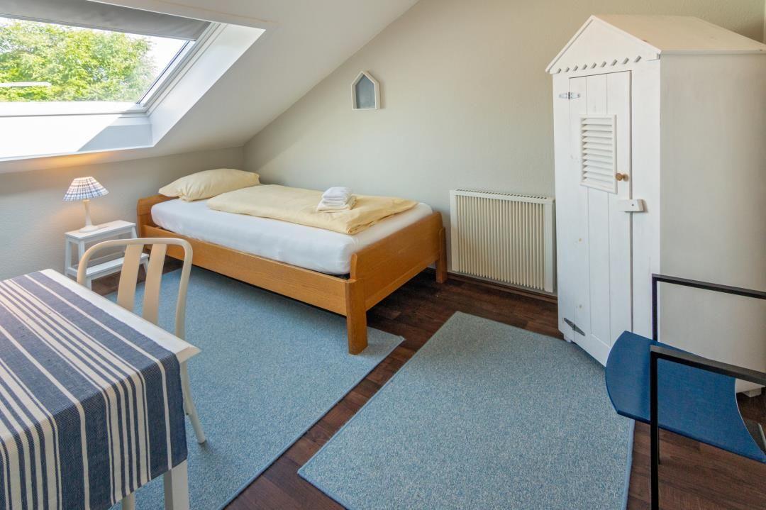 Zimmer mit Dachfenster, Bett, Schrank und Tisch mit Stühlen.