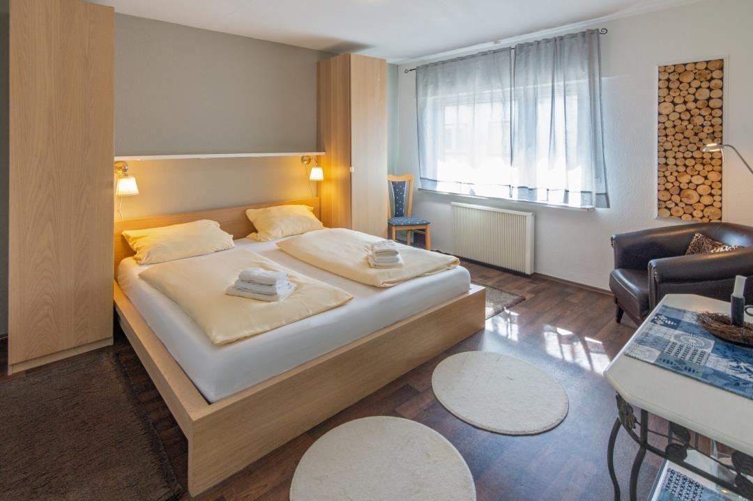 Schlafzimmer mit Doppelbett, Holzmöbeln und Fenster mit Vorhängen.