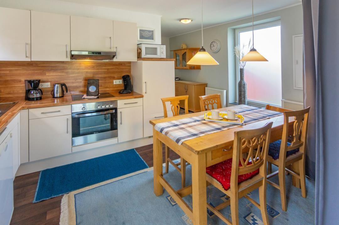Küche mit Essbereich, Holztisch, Stühle und Küchenzeile mit Herd und Kühlschrank.