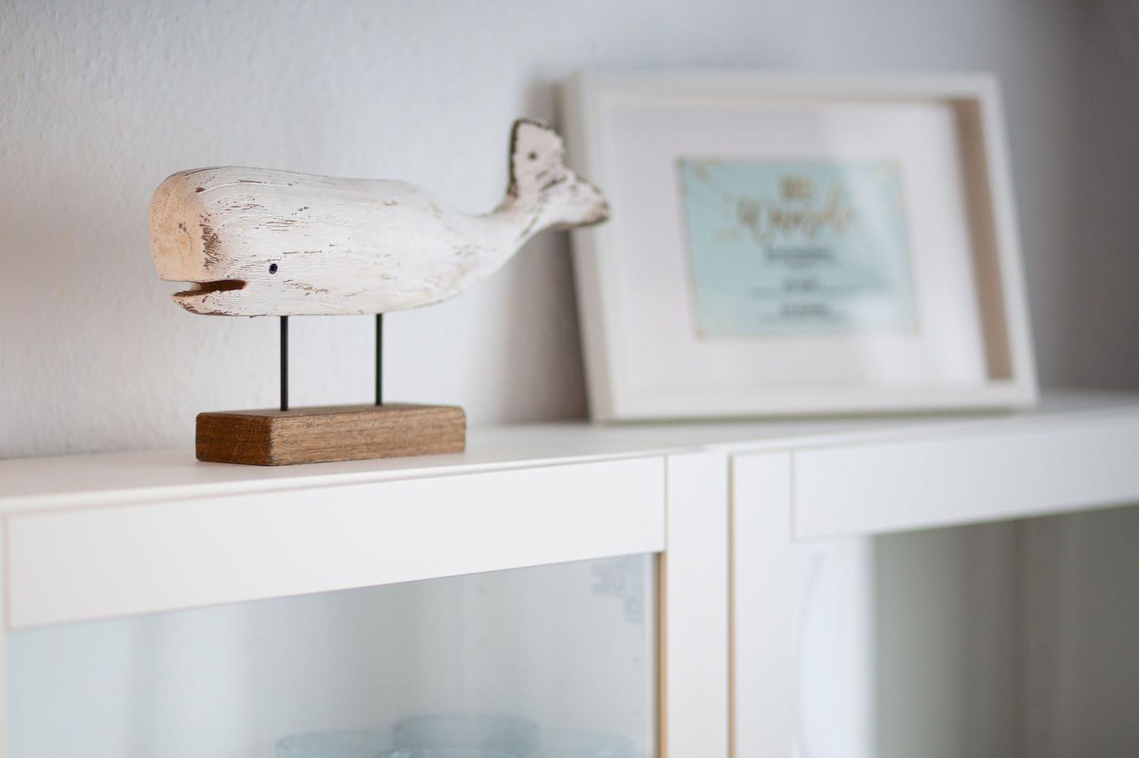 Holzfigur eines Walles auf einem weißen Regal neben einem Bilderrahmen.