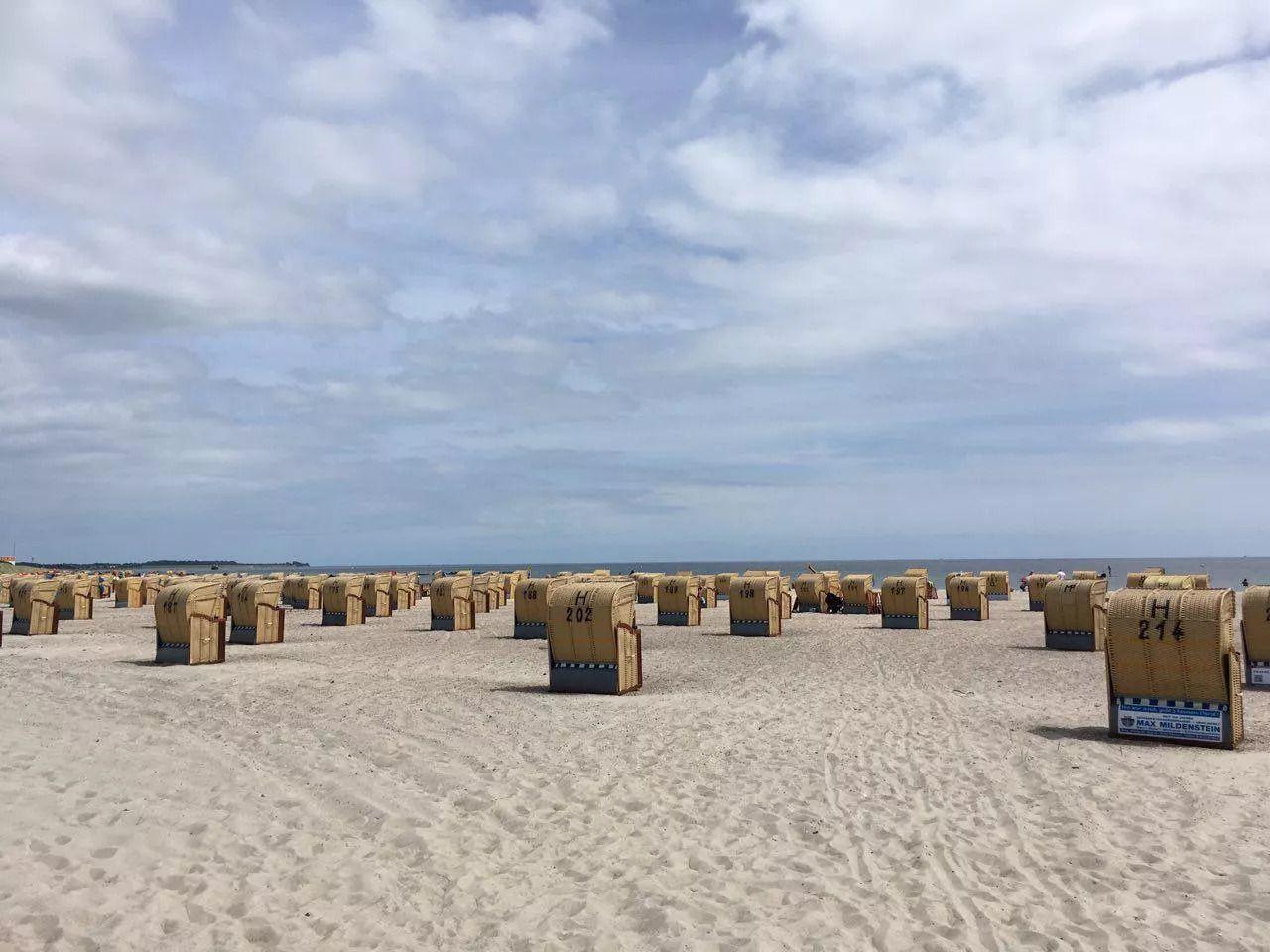 Strand mit vielen gelben Strandkörben und blauem Himmel.