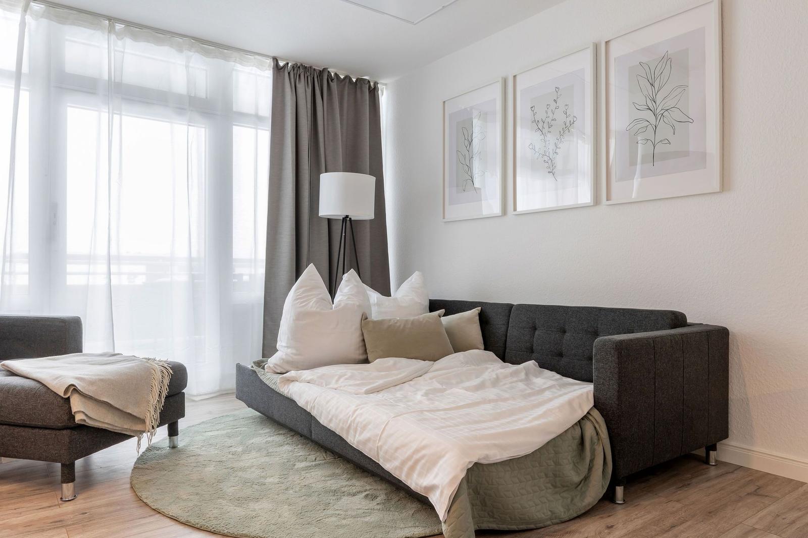 Schlafzimmer mit Sofa-Bett, Wandbildern und großem Fenster mit Blick.
