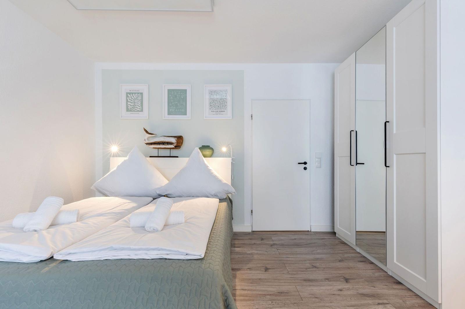 Schlafzimmer mit Bett, Kleiderschrank und Wandbildern.