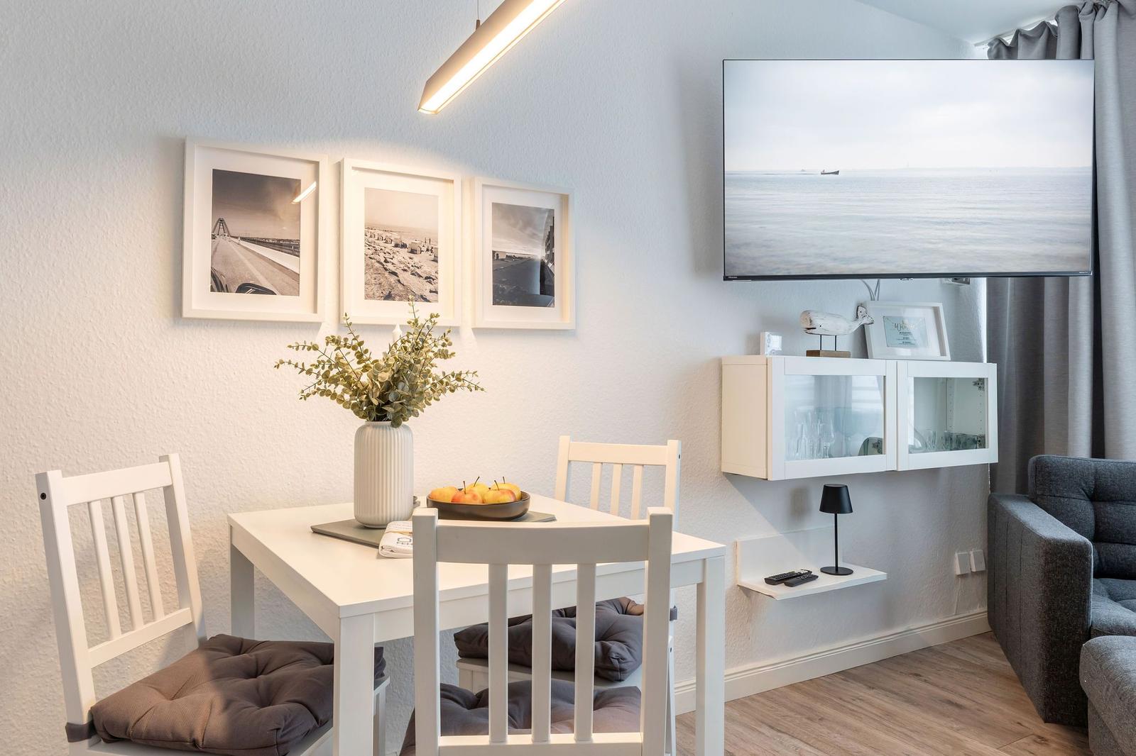 Essbereich mit Tisch, Stühlen und Fernseher an der Wand.