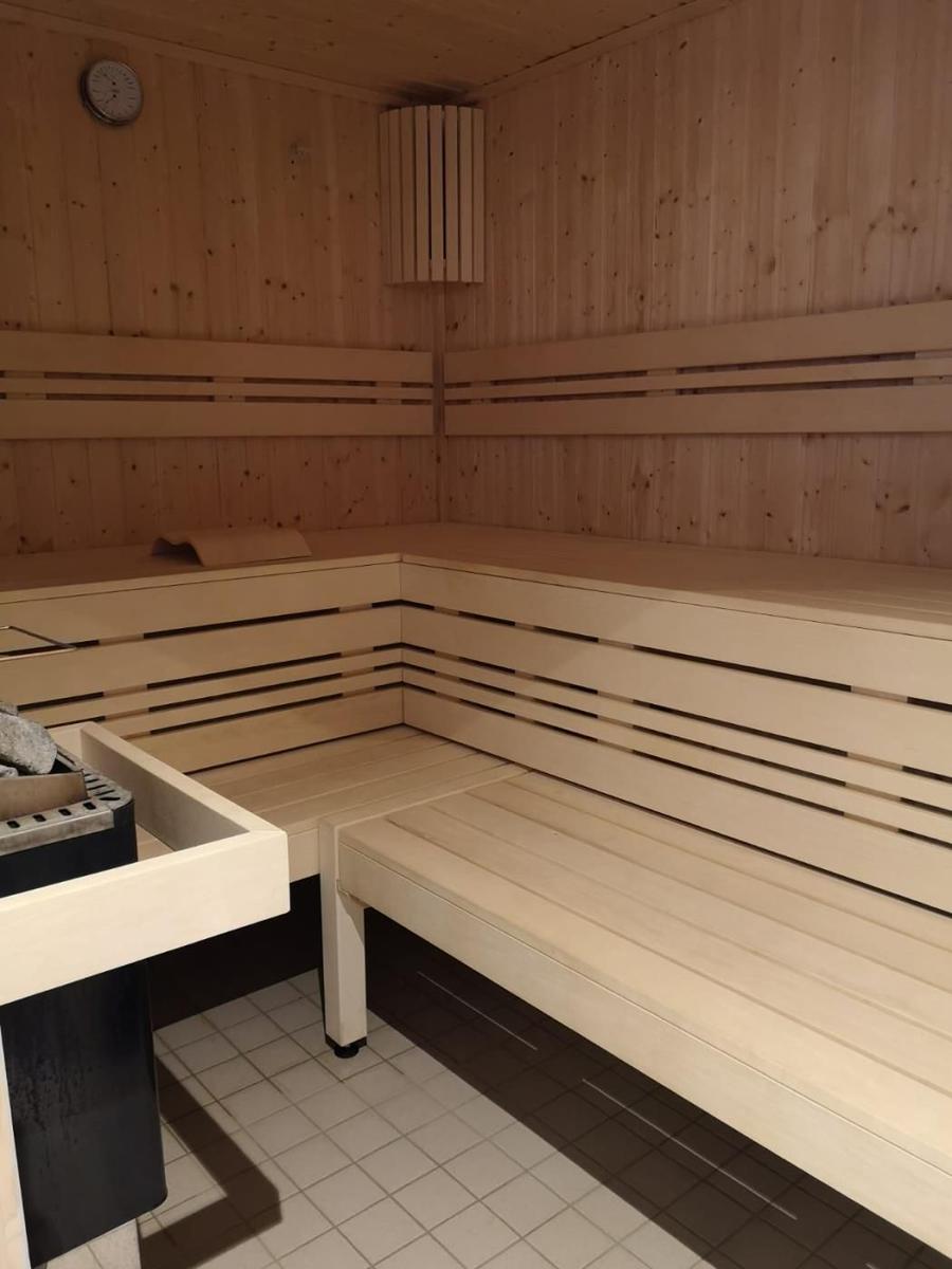 Sauna mit Holzbanken und Heizung. Bodenfliesen und Wanduhr sichtbar.