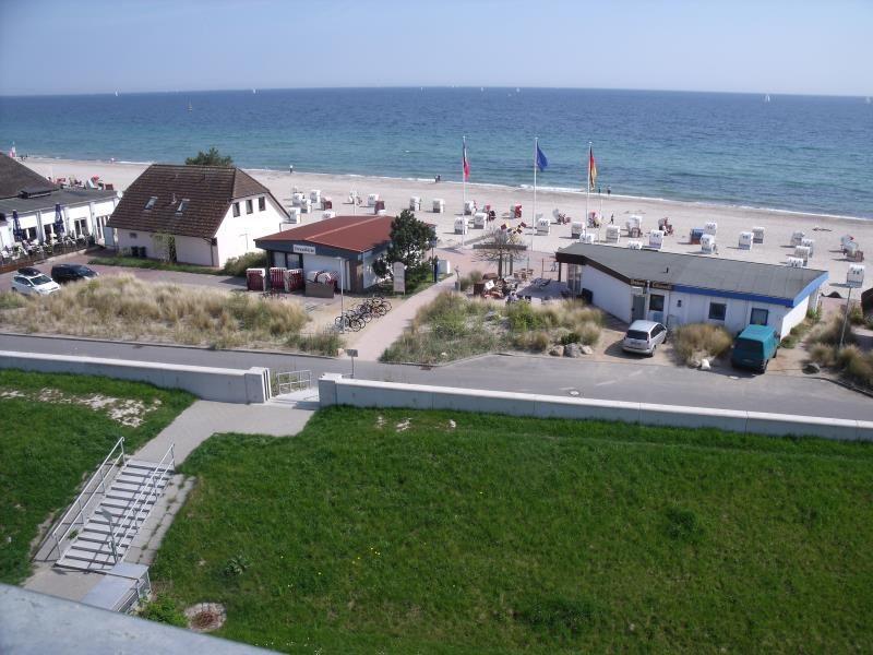 Strand mit Liegestühlen, Häuser und Grünflächen im Hintergrund.