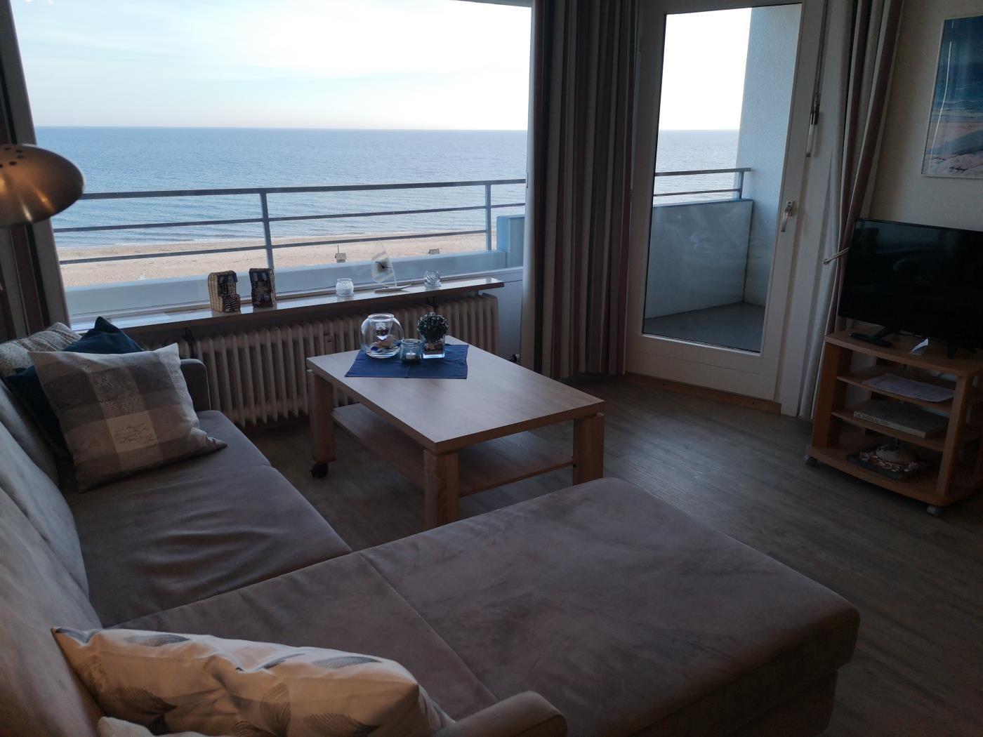 Wohnzimmer mit Sofa, Couchtisch und TV. Blick aufs Meer vom Balkon.