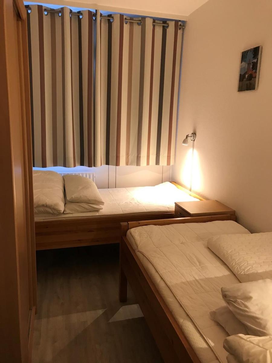 Zwei Einzelbetten mit Holzgestell und Bettwäsche. Streifenstore und Wandlampe.