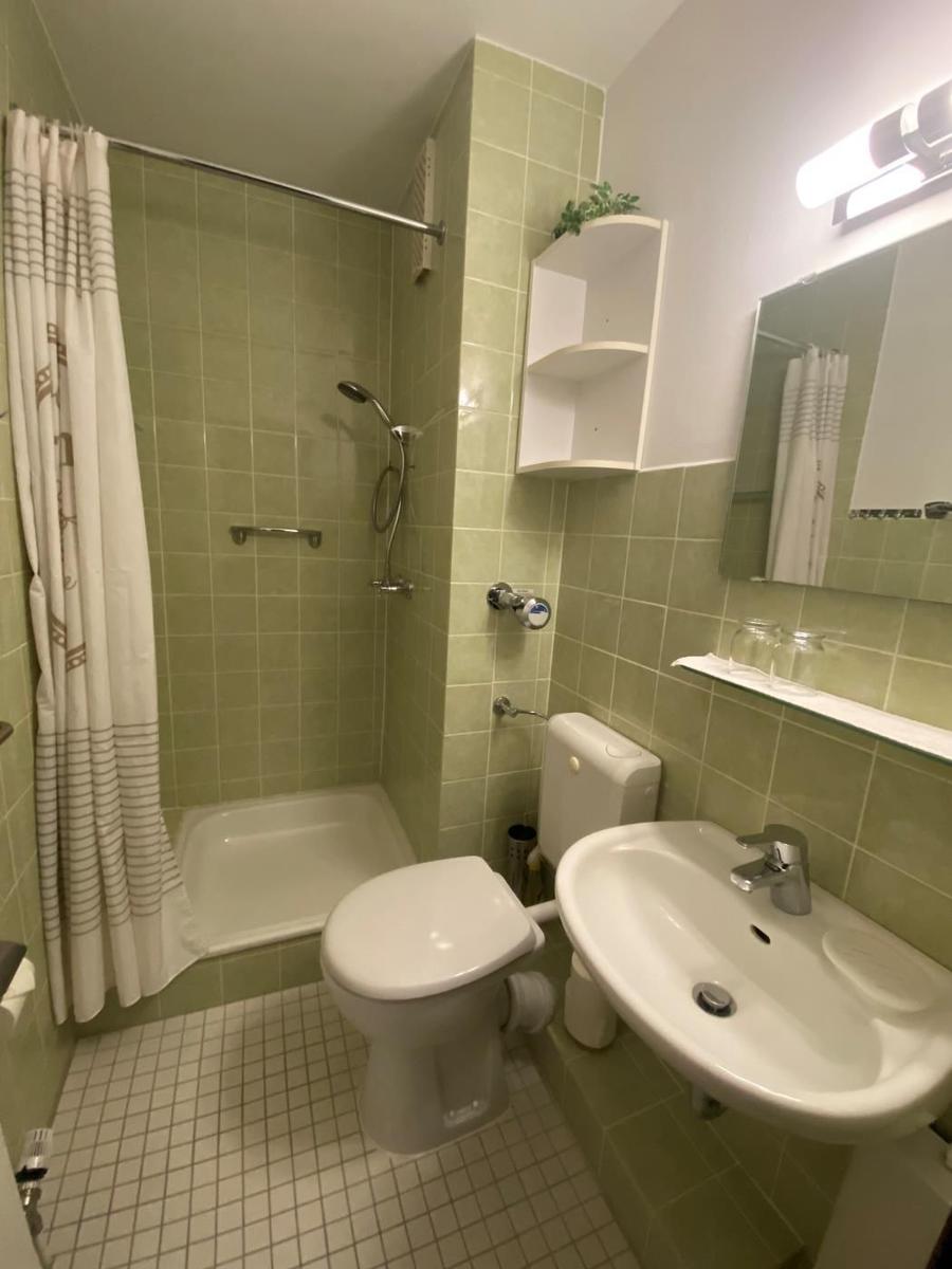 Badezimmer mit Dusche, Toilette und Waschbecken. Wandfliesen und Spiegel sichtbar.