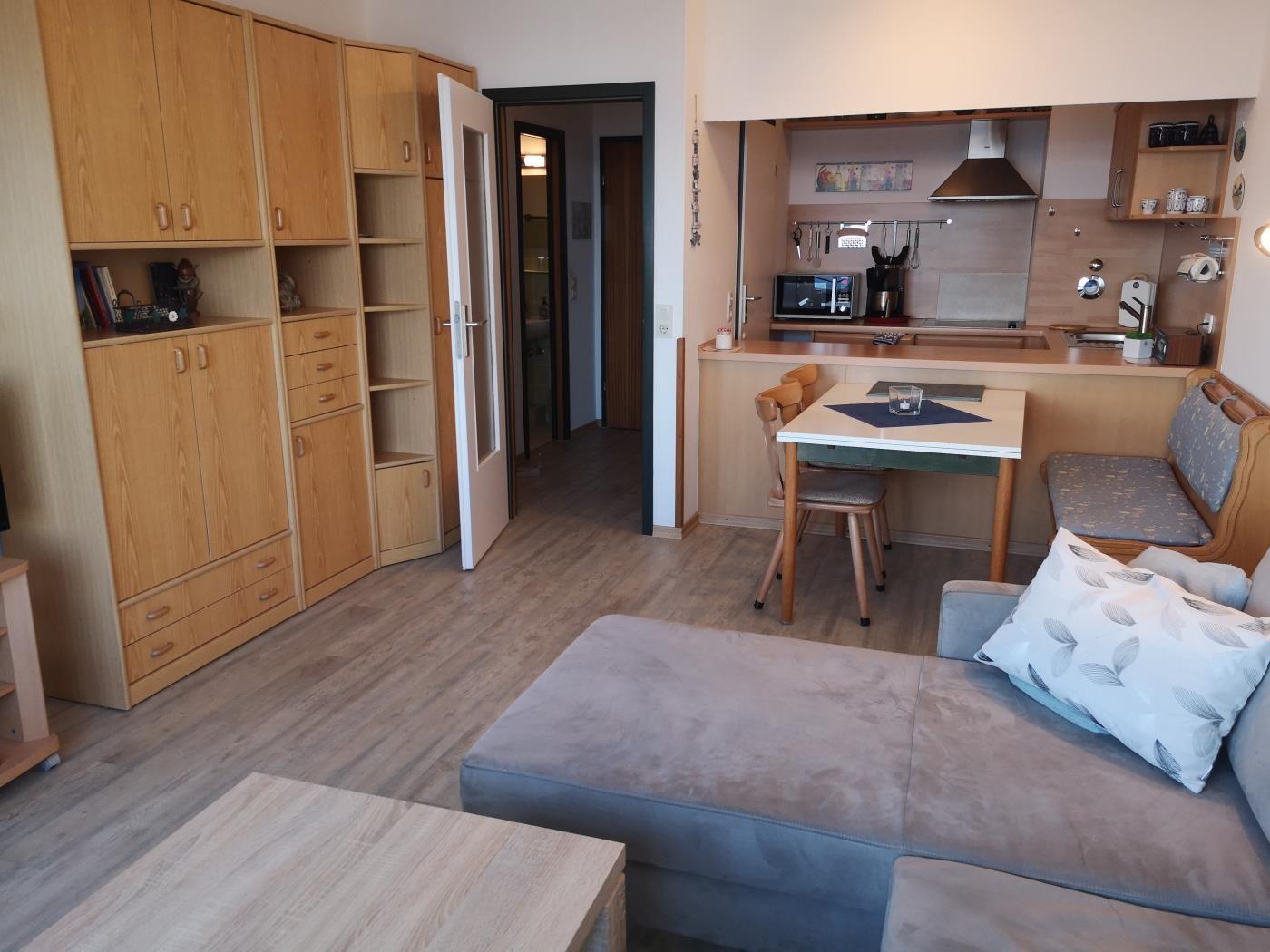 Wohnung mit Küche, Essplatz und Schlafbereich. Holzmöbel und helles Ambiente.