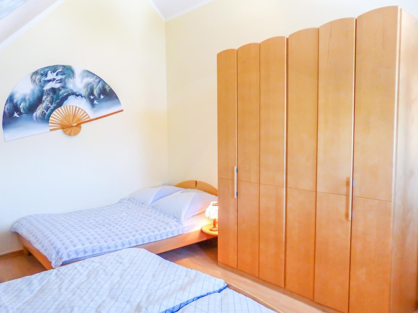 Zimmer mit zwei Betten, Holzschrank und Wandbild in Fächerform.