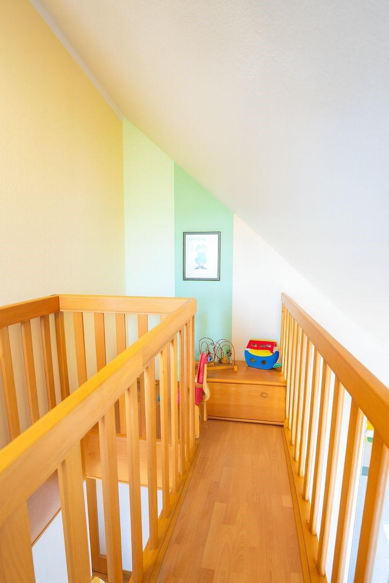Kinderzimmer mit Holzgeländer, farbigen Wänden und Spielzeug auf einem Schrank.