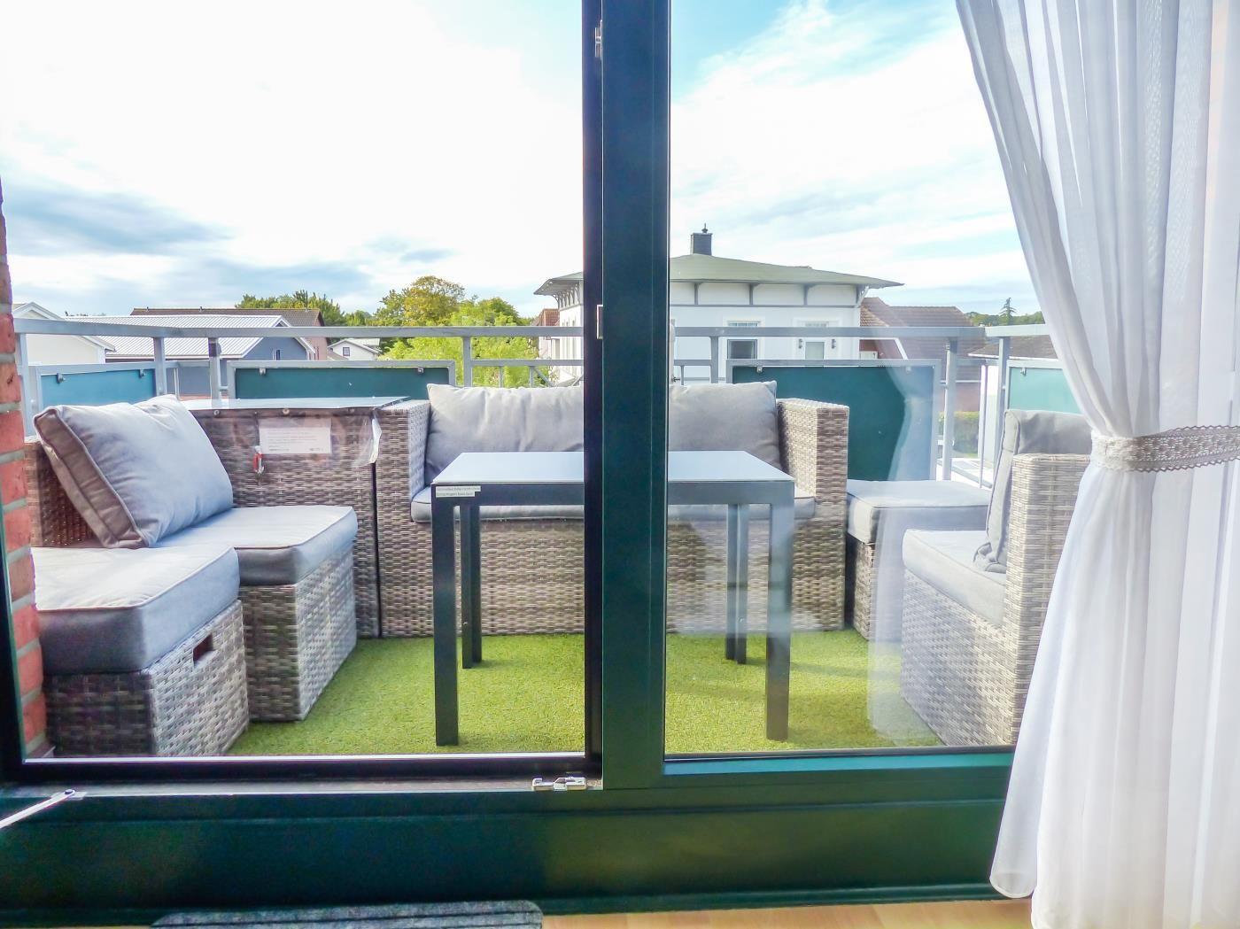 Terrasse mit Sitzgruppe und Tisch auf künstlichem Gras, Blick auf Wohnhäuser.