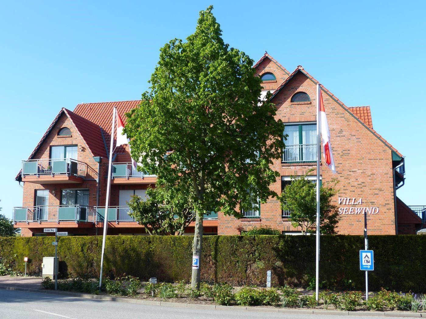 Villa Seewind mit rotem Dach und Balkonen. Vorderhof mit Bäumen und Hecke.