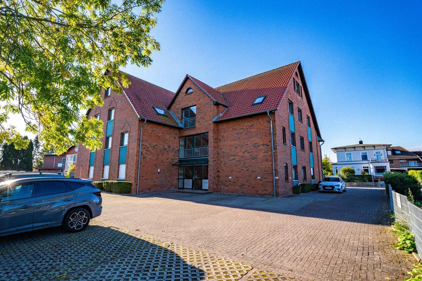 Rotes Backsteingebäude mit Dachterrassen und Parkplatz. Bäume und klare Himmel.