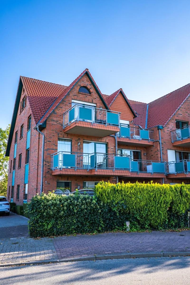 Rotes Backsteinhaus mit Balkonen und grünen Hecken im Vordergrund.