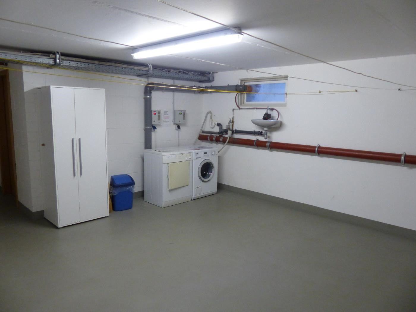 Waschraum mit Waschmaschine, Trockner und Spülbecken an der Wand.