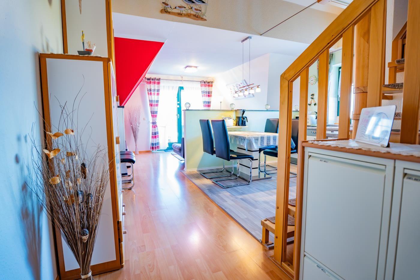 Haus mit Essbereich, Küchenzeile und Holzboden. Rote Wand und Fenster mit Vorhängen.