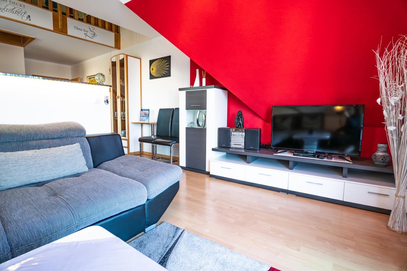 Wohnzimmer mit Sofa, Fernseher und roter Wand unter Dachschräge.