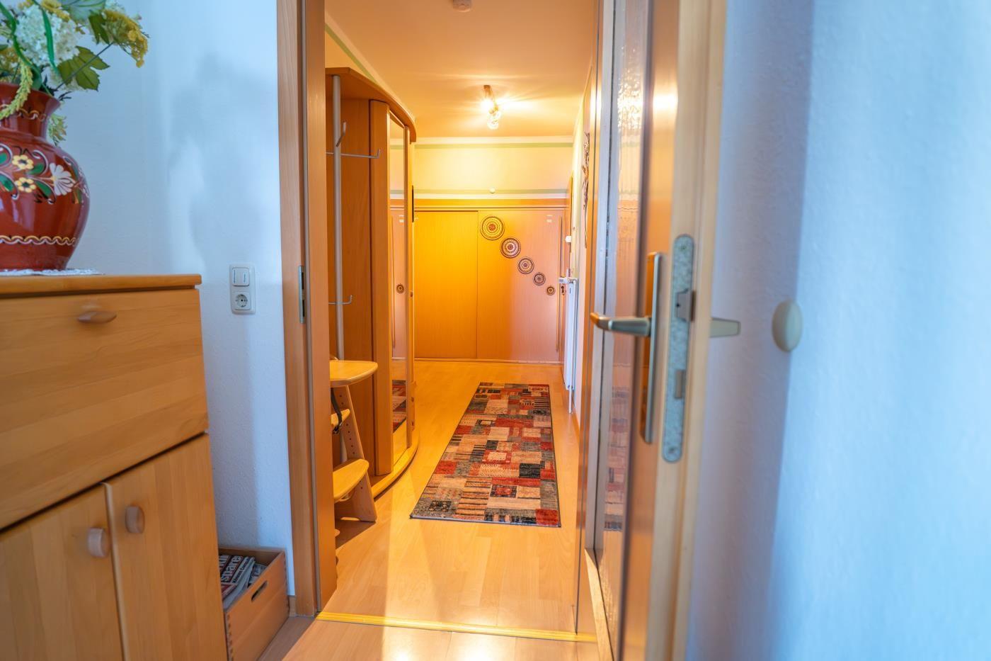 Flur mit Holzboden, Teppich und Schrank. Blumenvase auf Möbel.