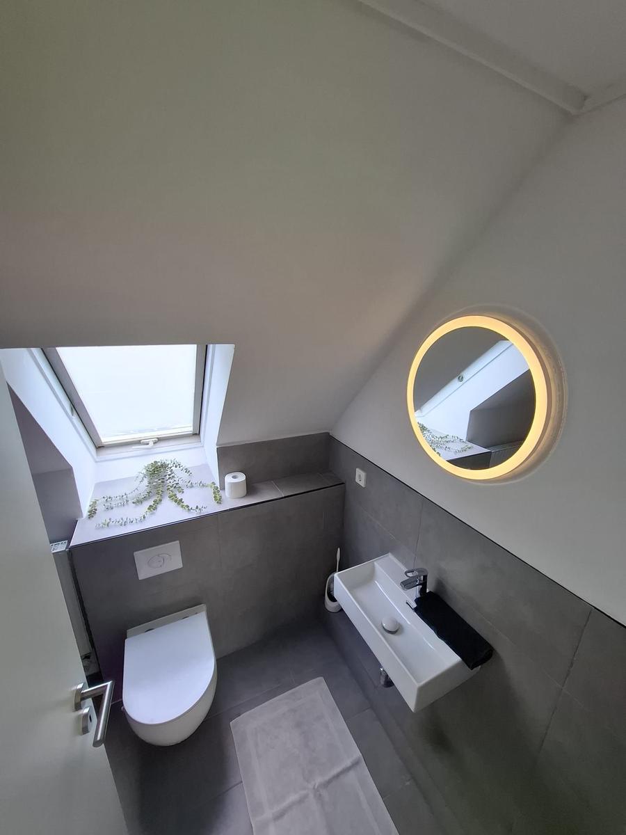 Badezimmer mit Dachfenster, runden Spiegel und Toilette.