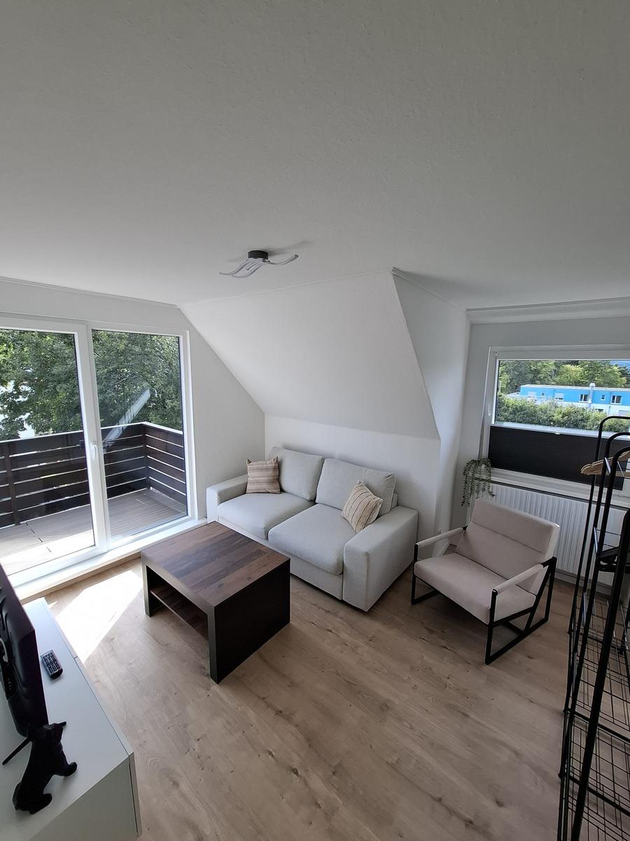 Wohnzimmer mit Sofa, Sessel und Tisch. Balkon und Fenster mit Blick.