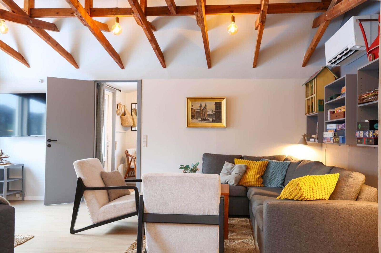 Living room with wooden beam ceiling, sofa and armchairs. Shelving with toys and picture on wall.