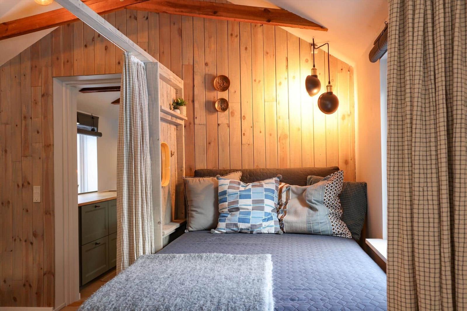 Bedroom with wooden wall, bed, and curtains. Two lamps hang on the wall.