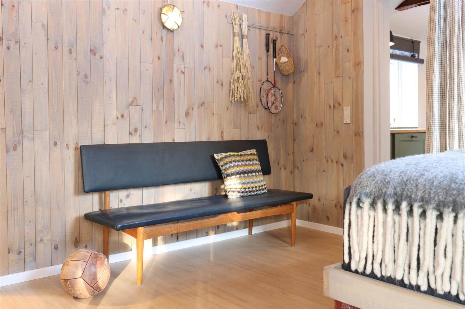 A room with wooden walls, bench, pillow, badminton rackets, and pillow on the bed.