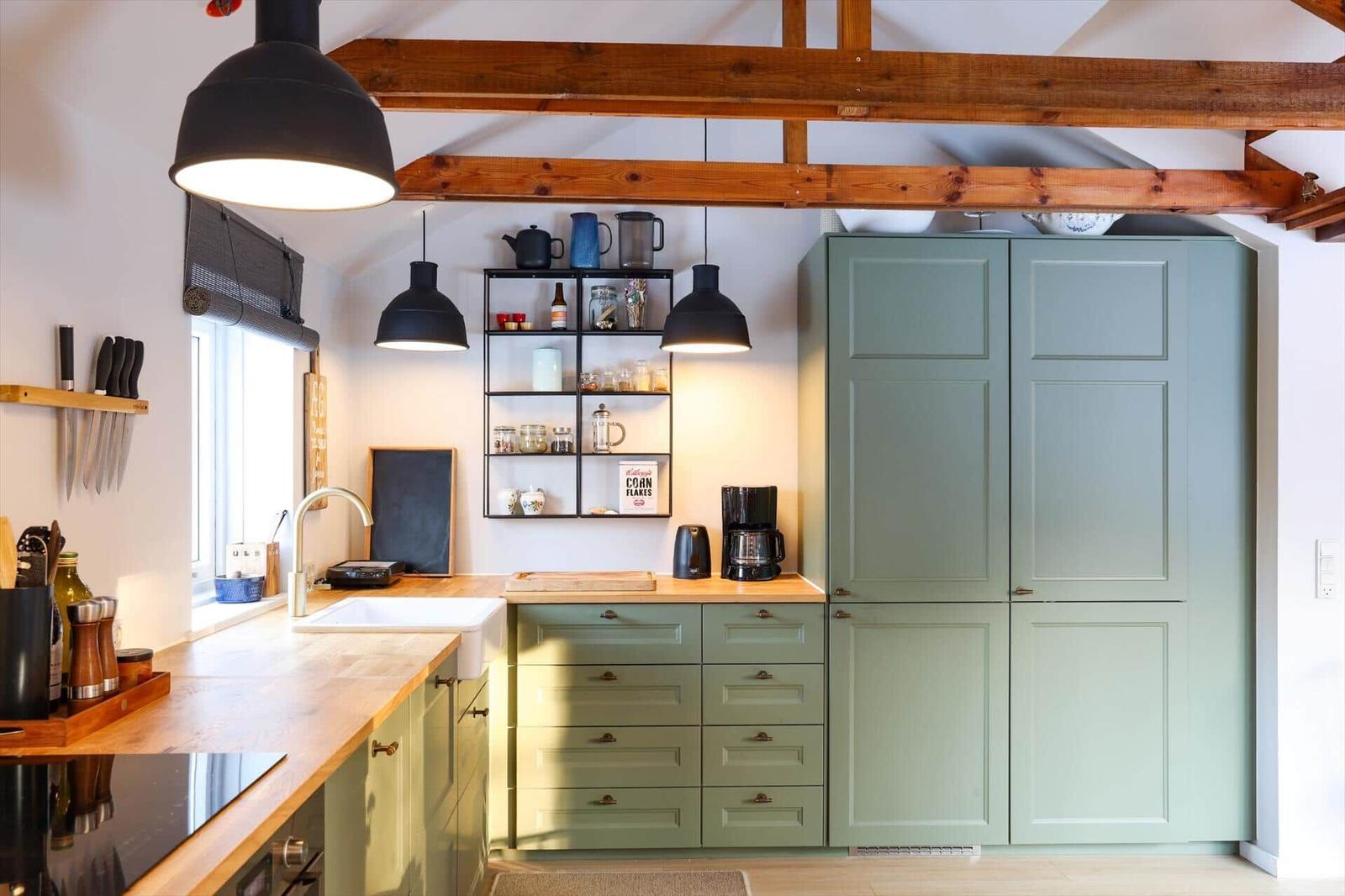 Kitchen with green cabinets, wooden countertop, and black pendant lights under wooden beams.