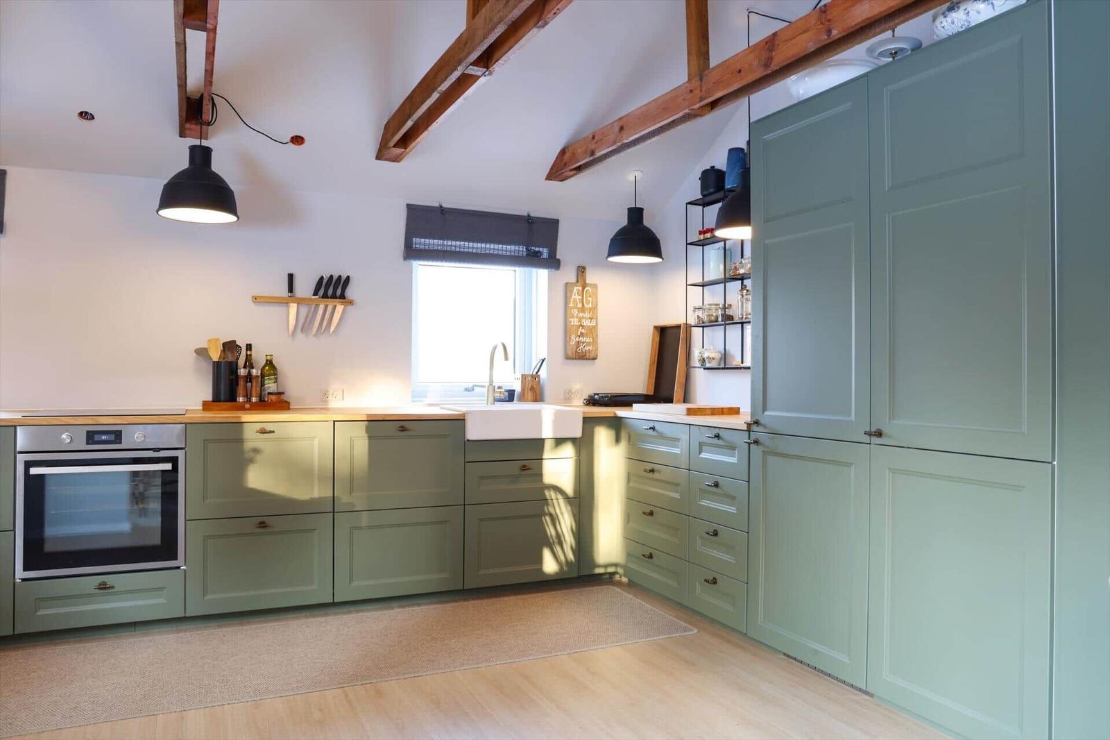 Kitchen with green cabinets, wooden beams, and a window above the sink.
