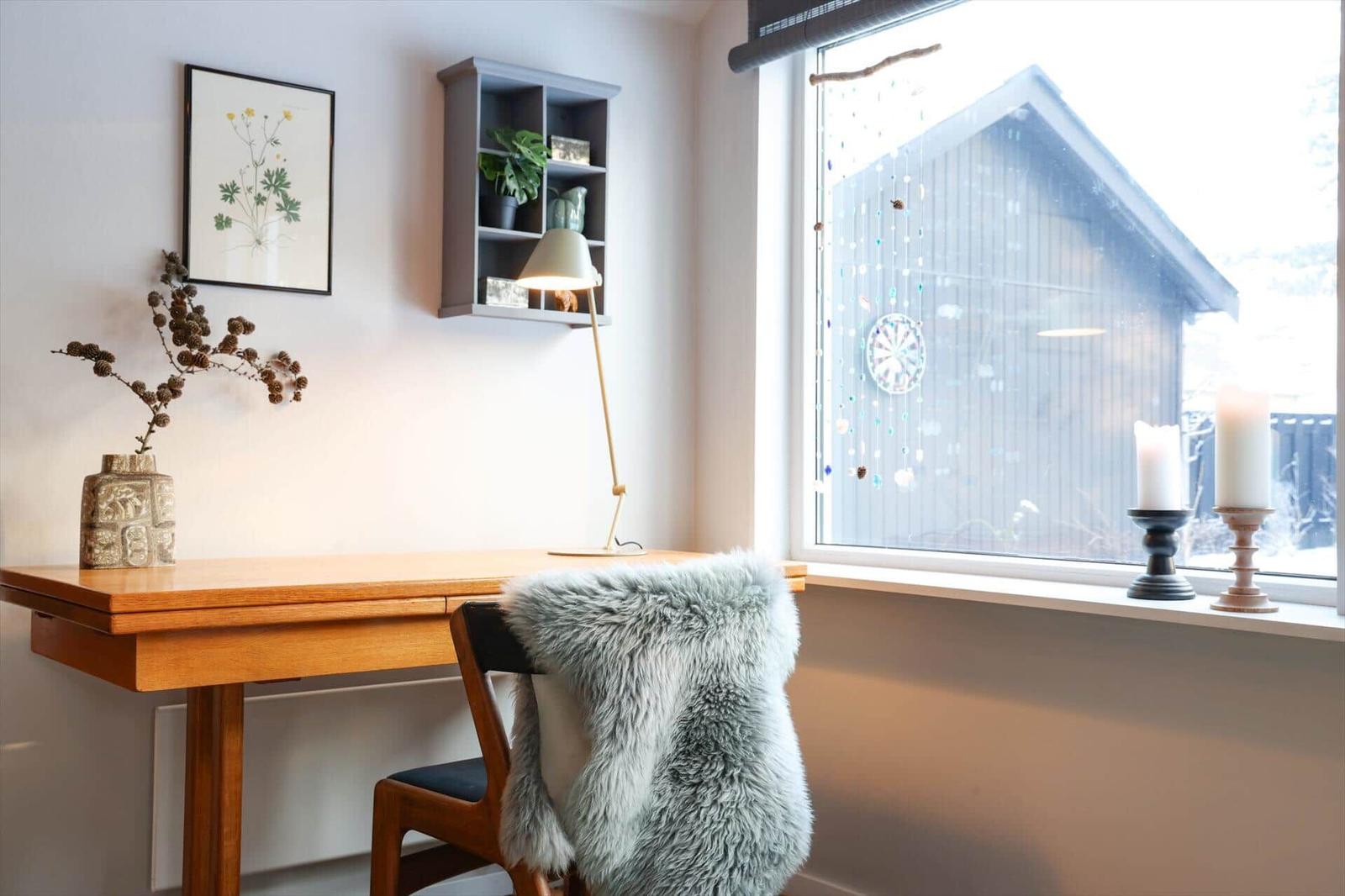 Desk with chair and fur throw by large window with candles and decor.