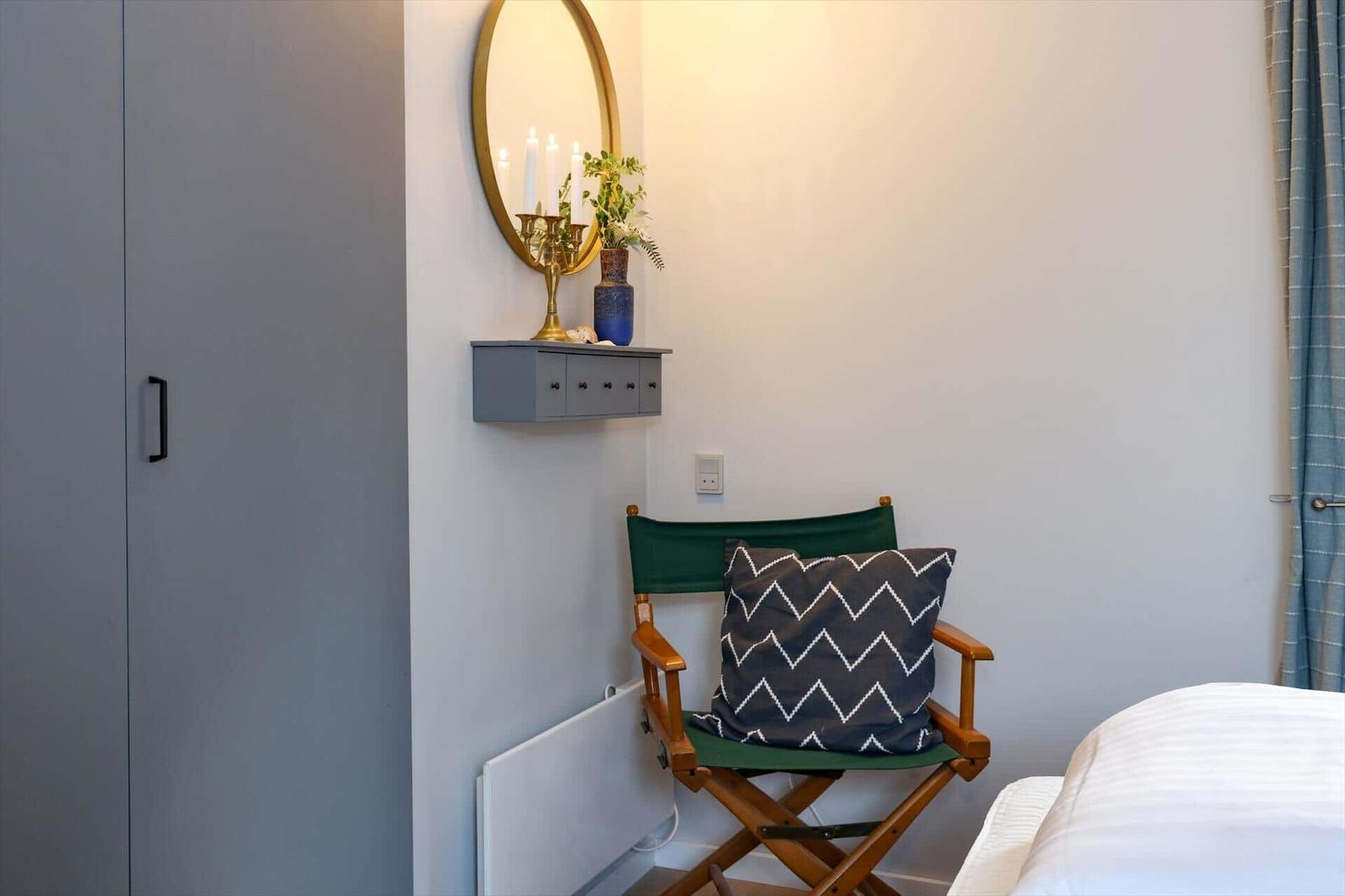 A bedroom with chair, mirror, and wardrobe against the wall.