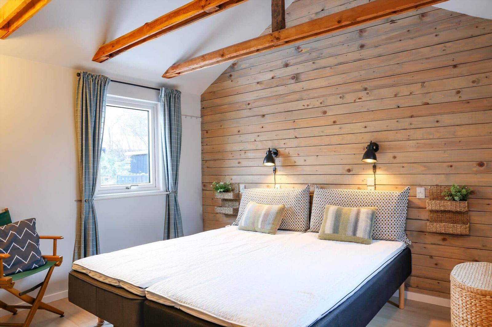 Bedroom with wooden wall, bed, window and chairs.