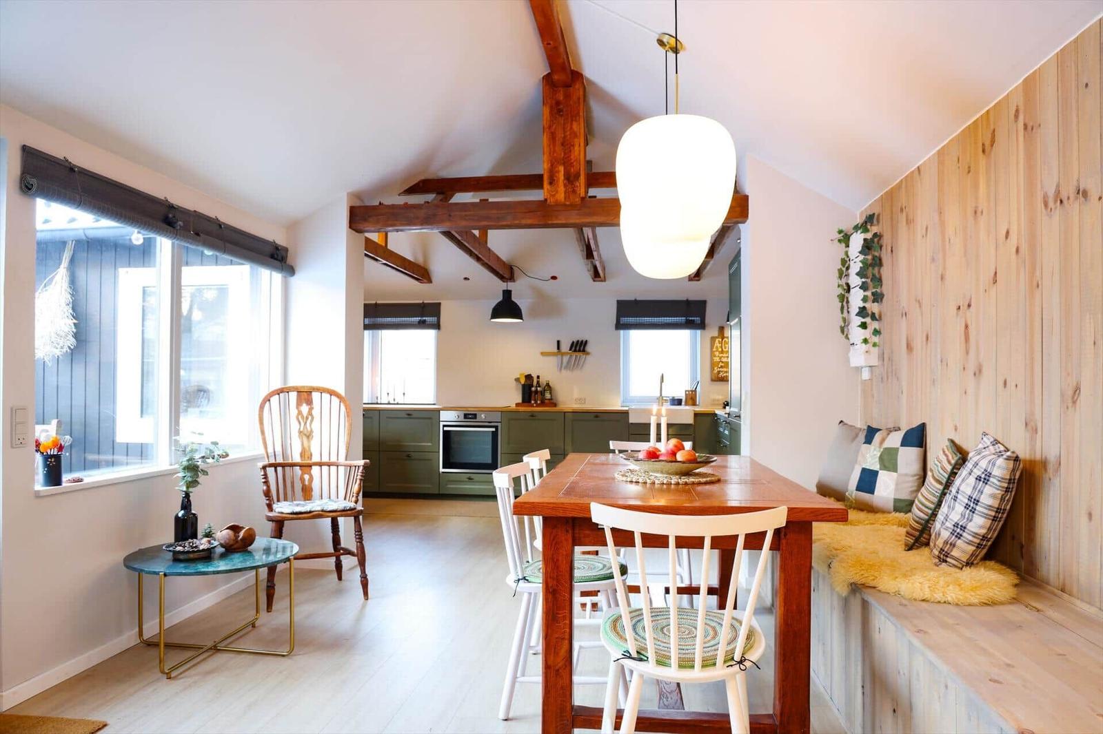 Dining area with wooden table, bench, and kitchen area in the background.