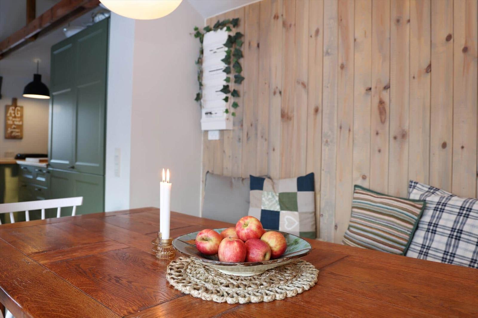 Wooden table with apple bowl and candle against wooden wall with cushions.